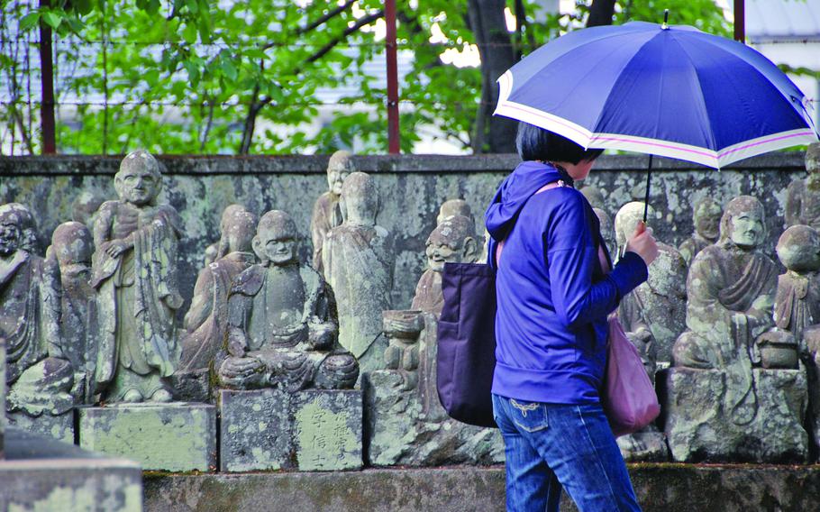 A person holding an umbrella walks by a carved wall.