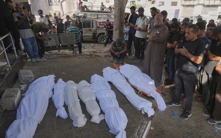 Bodies wrapped in white cloth while mourners pray over the bodies.