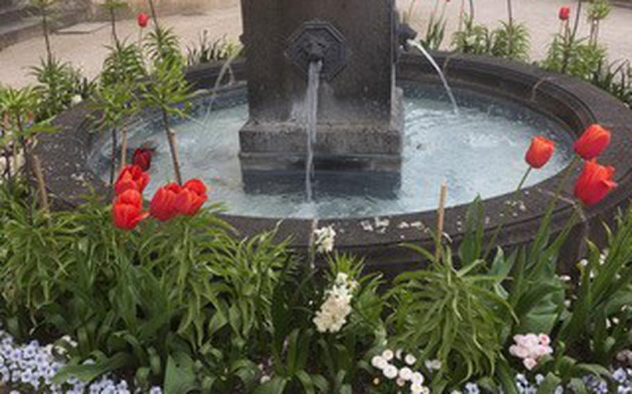 A smaller fountain surrounded by flowers is situated near the pergola garden at Schloss Stolzenfels. The spot offers an expansive view of the Rhine River valley near Koblenz, Germany.