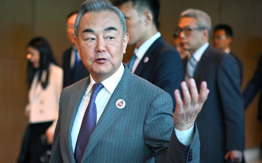 Wang Yi gestures with one hand with his lips parted slightly as others walk in the background.