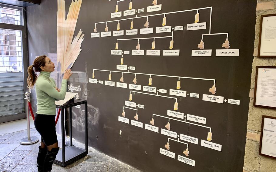 An Italian woman stands in front of a wall decorated with a large family tree.
