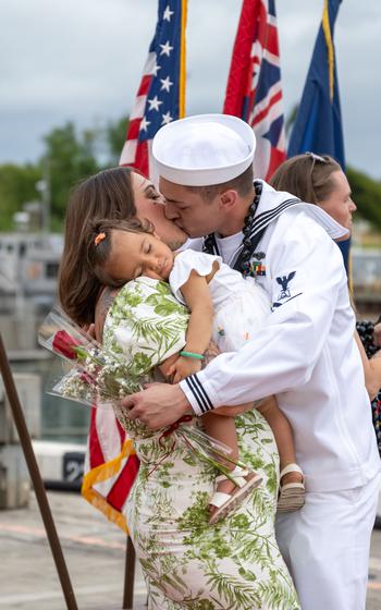 A sailor kisses a loved one and embraces a child.