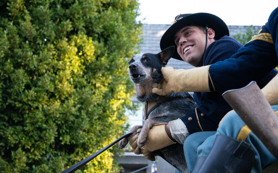A soldier holds Doc Holliday, and another scratches the dog’s neck.