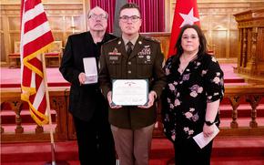 Martin and his parents hold the medals with flags behind them.