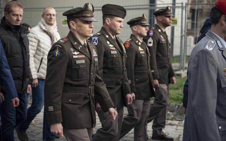 A line of soldiers in service uniforms march between German civilians
