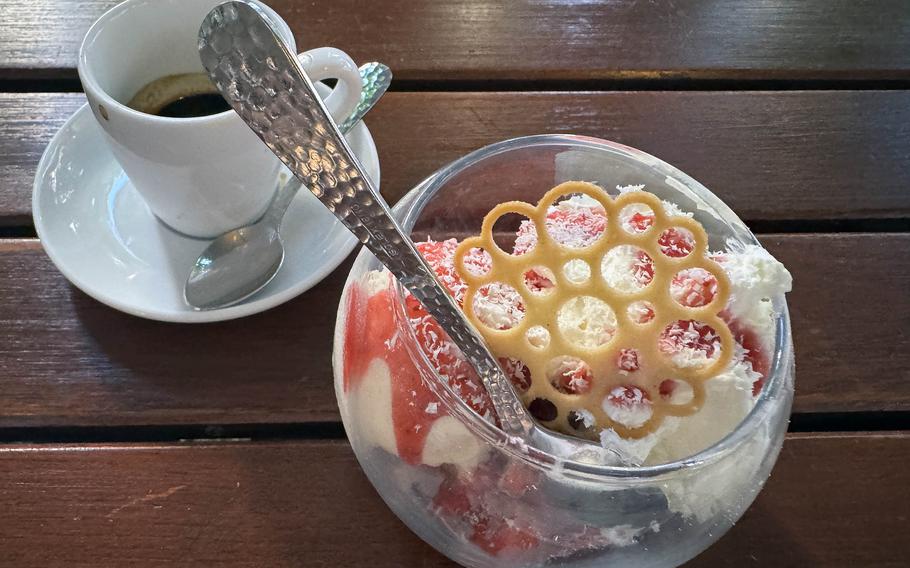A bowl of strawberries topped with with vanilla ice cream and whipped cream and a cup of espresso.
