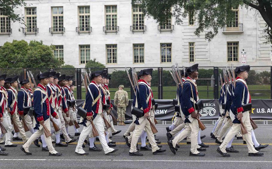 Soldiers in red, white and blue colonial uniforms marching.