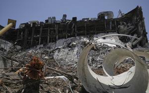 Debris is piled in front of a severly damaged multi-story building.