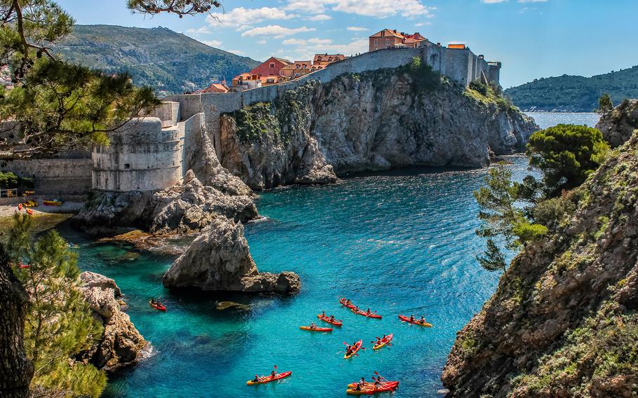 Kayakers paddle through the crystal-clear blue water below the walls surrounding Dubrovnik, Croatia.