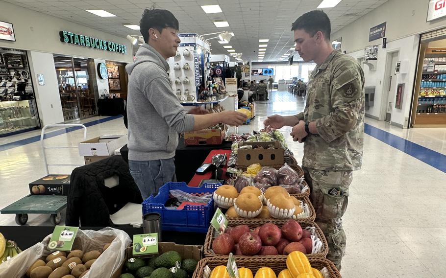 A Korean man hands a small fruit to a U.S. airman. 