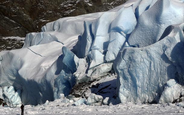 A person stands on a frozen lake to take photos of a glacier.