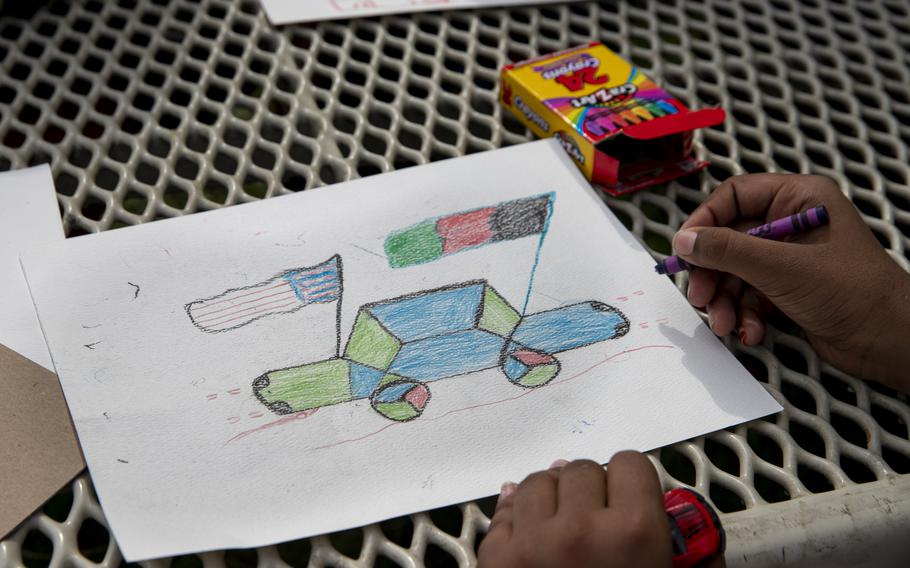 An Afghan child draws a car with the American and Afghanistan flag at a children’s activity event held by non-governmental charities on Ft. McCoy, Wisconsin, Aug. 31, 2021.