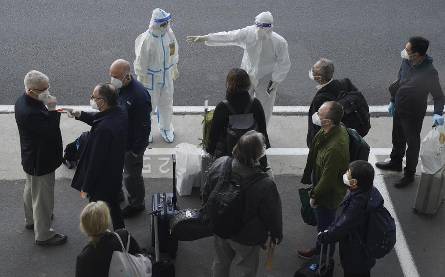 In this Jan. 14, 2021, file photo, a worker in protective coverings directs members of the World Health Organization (WHO) team on their arrival at the airport in Wuhan in central China’s Hubei province. China’s Foreign Ministry on Thursday, Oct. 14, warned against what it called possible “political manipulation” of a renewed probe by the World Health Organization into the origins of the coronavirus, while saying it would support the international body’s efforts.