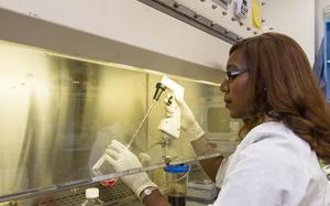 A doctor wearing protective gear looks at liquid in a container.