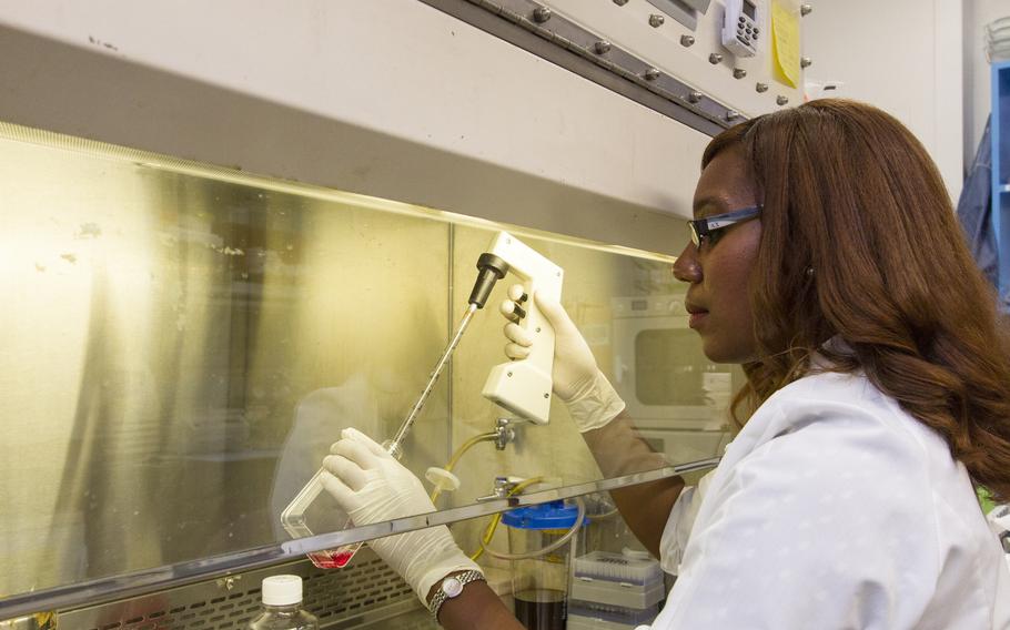 A doctor wearing protective gear looks at liquid in a container.