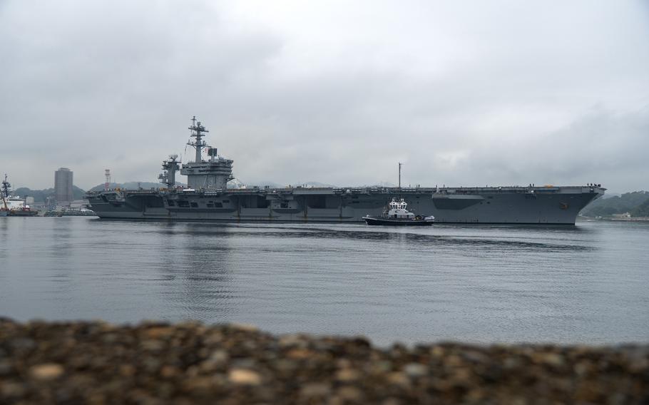 A tugboat escorts an aircraft carrier through a bay.
