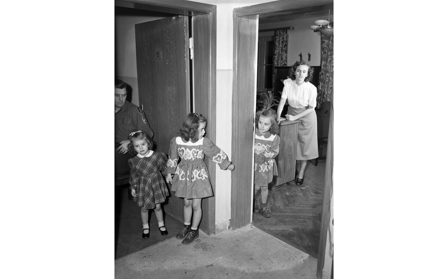 Glenda Lee, 7, Billie Joe, 6, and Sandra Elizabeth, 3, daughters of M. Sgt. William F. Garland, of Hq Co., 18th Inf., and his wife, Helen, play hide-and-seek in the family’s new apartment, one of the 156 newly constructed apartment units for service members and their families in Aschaffenburg, as their father and mother look on.