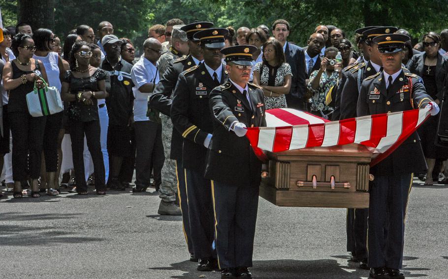 A military honor guard carries a casket before onlookers.