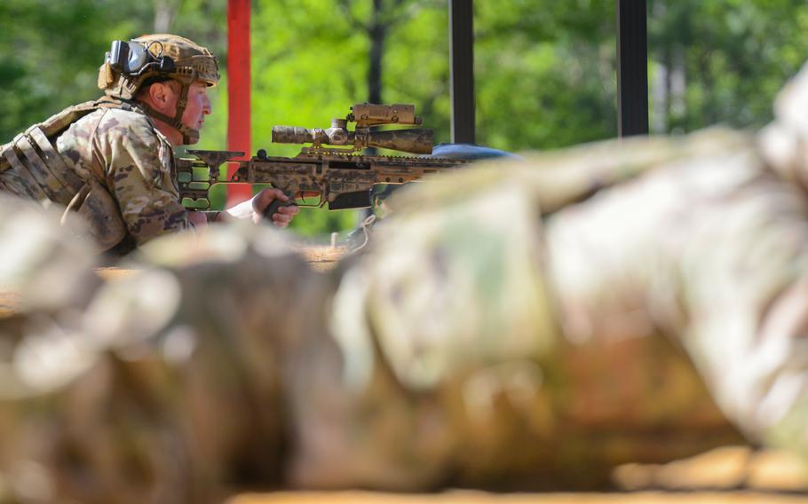 An out-of-focus sniper lies prone in the foreground while an in-focus sniper holds a rifle next to him, farther from the camera.