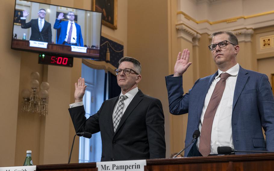 Two men in suits raise their right hands to be sworn in before testifying at a congressional hearing.
