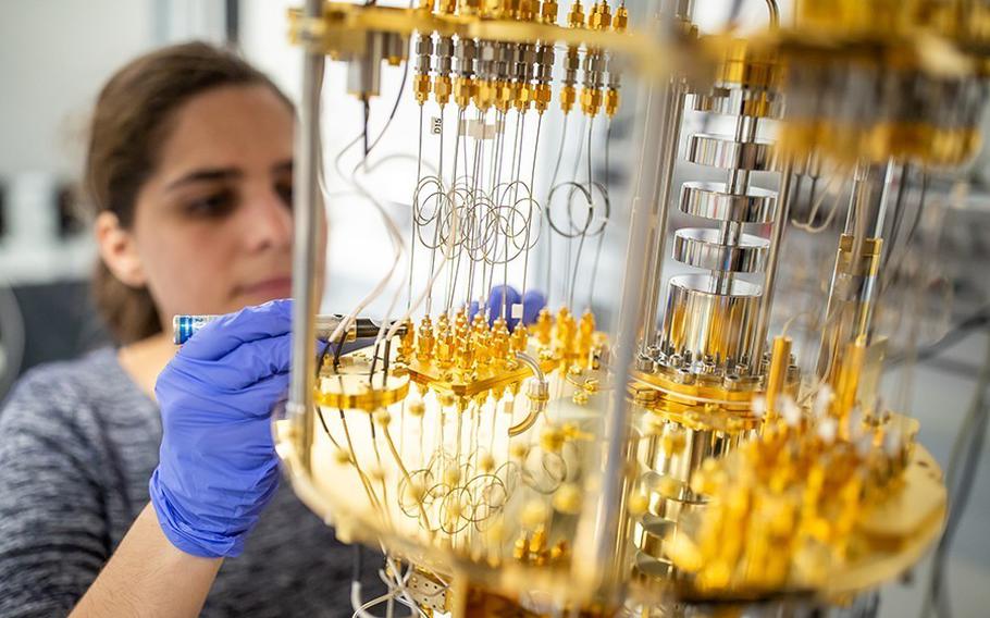 A scientist wearing blue gloves works on a complex quantum computing device with gold and metallic components in a laboratory setting.