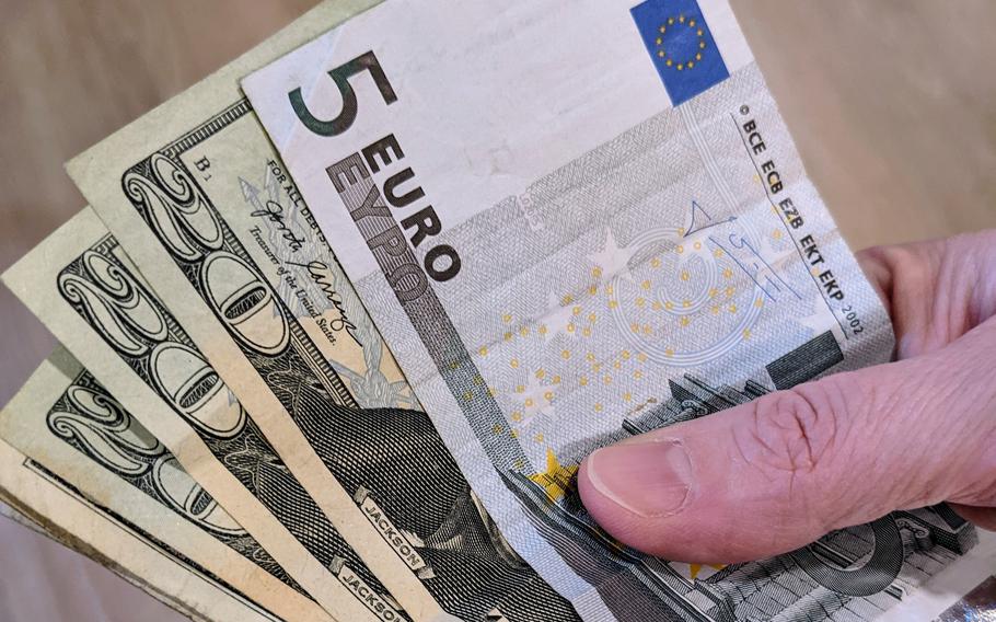 A hand displays several euro and U.S. dollar notes.