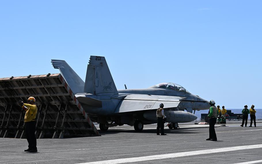 Several sailors stand near a fighter jet on an aircraft carrier deck.