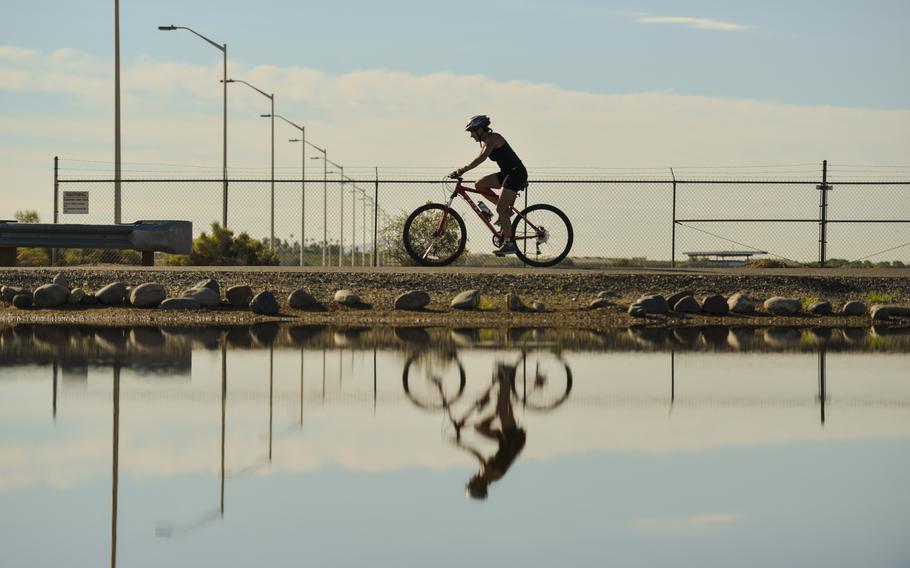 A pool of water reflects a triathlete riding a bike at Luke Air Force Base, Ariz., on Aug. 19, 2017. 