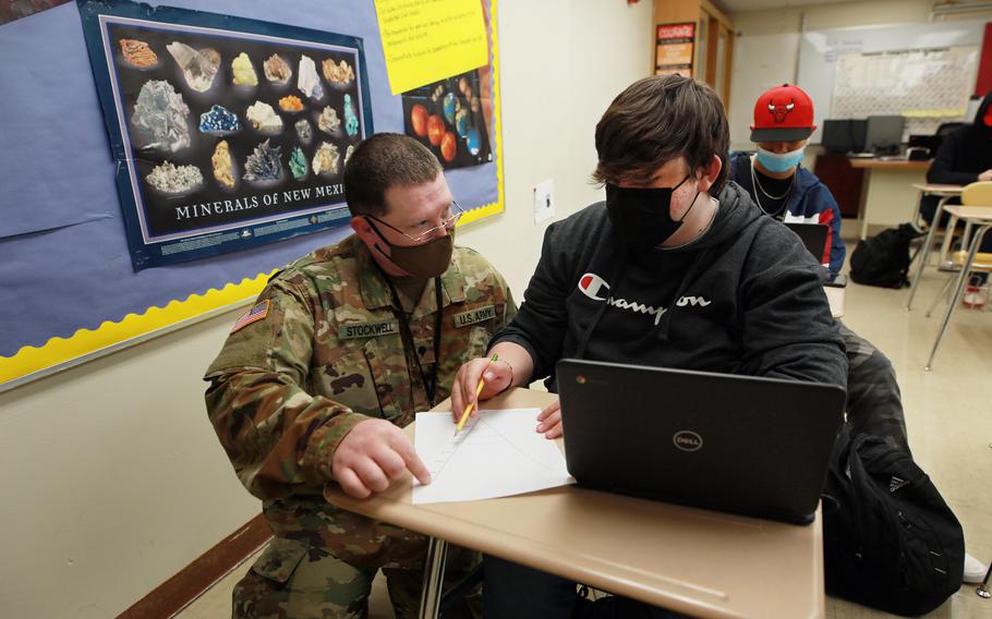 New Mexico Army National Guard specialist Michael Stockwell kneels while helping Alamogordo High School freshman Aiden Cruz with a geology assignment, at Alamogordo High School,Tuesday, Feb. 8, 2022, in Alamogordo, N.M. 