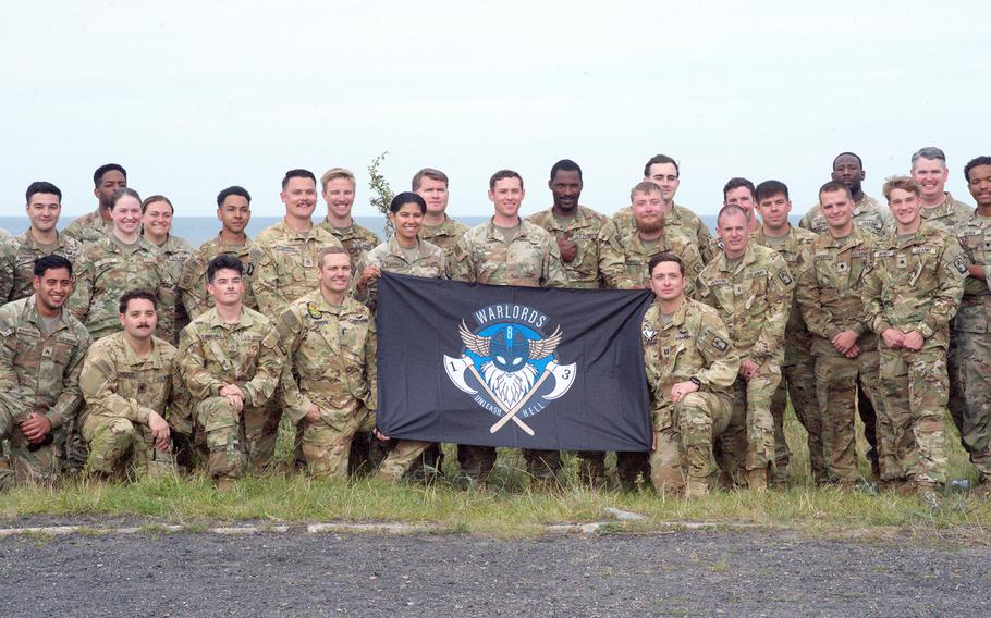 Soldiers hold a flag and pose for a photo.