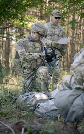 Two soldiers on patrol, one peers into a tracking device.
