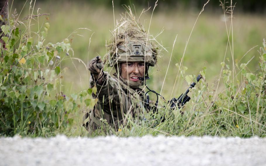 A cadet points as she guides a platoon through a field while training.