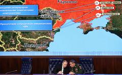 Russian President Vladimir Put, left, and Russian General Staff Valery Gerasimov talk to each other during an extended meeting of the Russian Defense Ministry Board at the National Defense Control Center with a Russian military map showing the alleged deployment of U.S. private military contractors in eastern Ukraine in the background in Moscow, Russia, Tuesday, Dec. 21, 2021. The Russian president on Tuesday reiterated the demand for guarantees from the U.S. and its allies that NATO will not expand eastward, blaming the West for current tensions in Europe. (Mikhail Tereshchenko, Sputnik, Kremlin Pool Photo via AP)