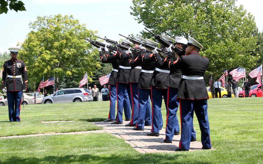 A row of Marines aiming their rifles at a park in salute.