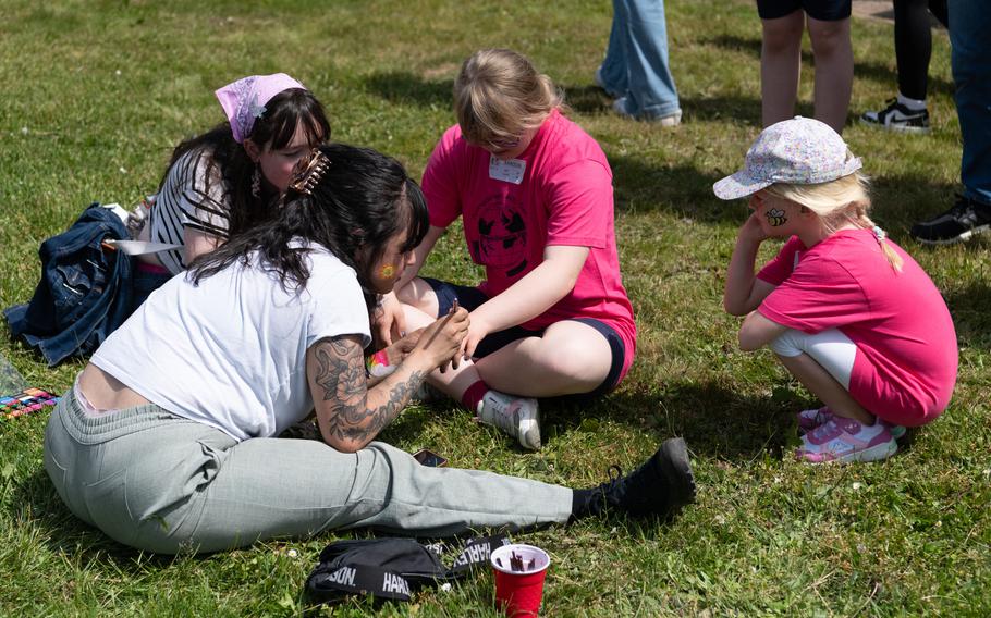 A woman sits in the grass next to three children as she paints one of their hands. 