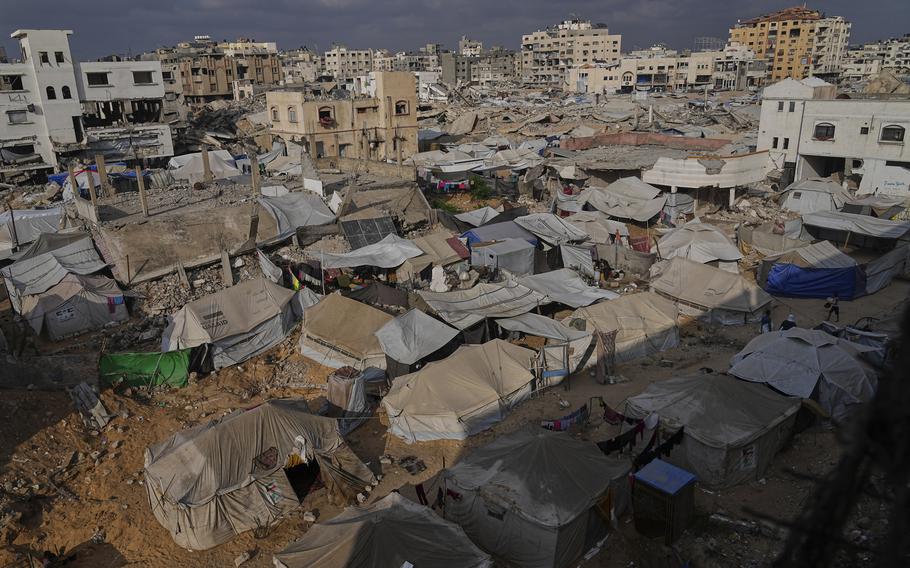 Rows of tents in the foreground with ruined buildings in the background.