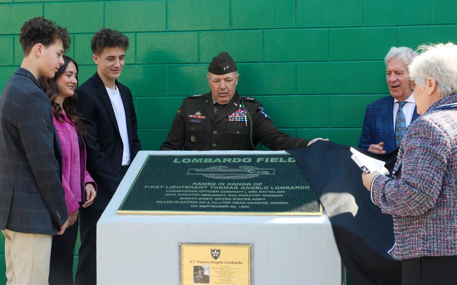 A general stands behind a plaque reading “Lombardo Field” as family members look on.