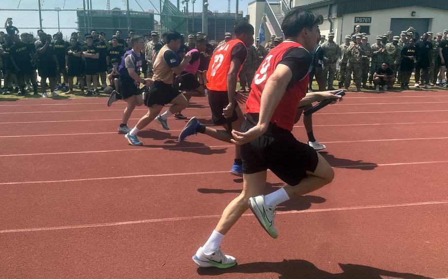 U.S. and South Korean soldiers in exercise clothing run on a track with other soldiers in the background lining the track to watch.