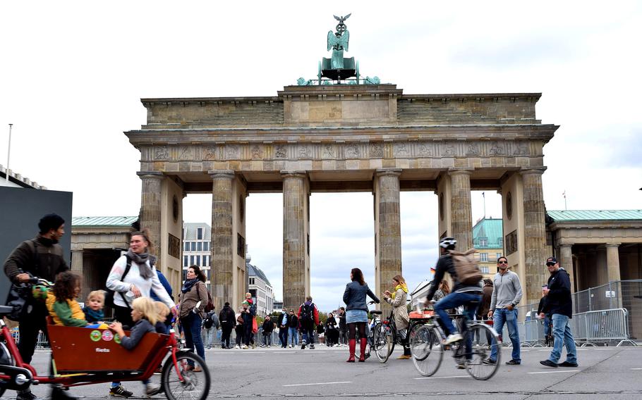 Tourists and Berliners stream past and through the Brandenburg Gate, which in 1987 served as the backdrop for Ronald Reagan’s famous “Tear Down This Wall” speech. A thin cobblestone strip in the foreground reveals the outer wall’s former path. 