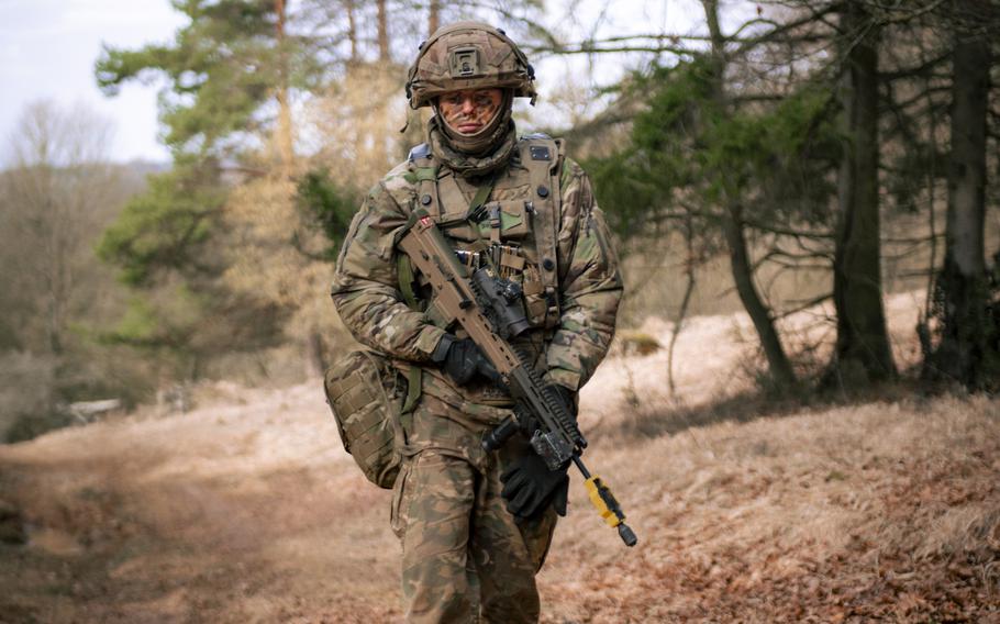 A British soldier in uniform walks along a dirt path holding a weapon.