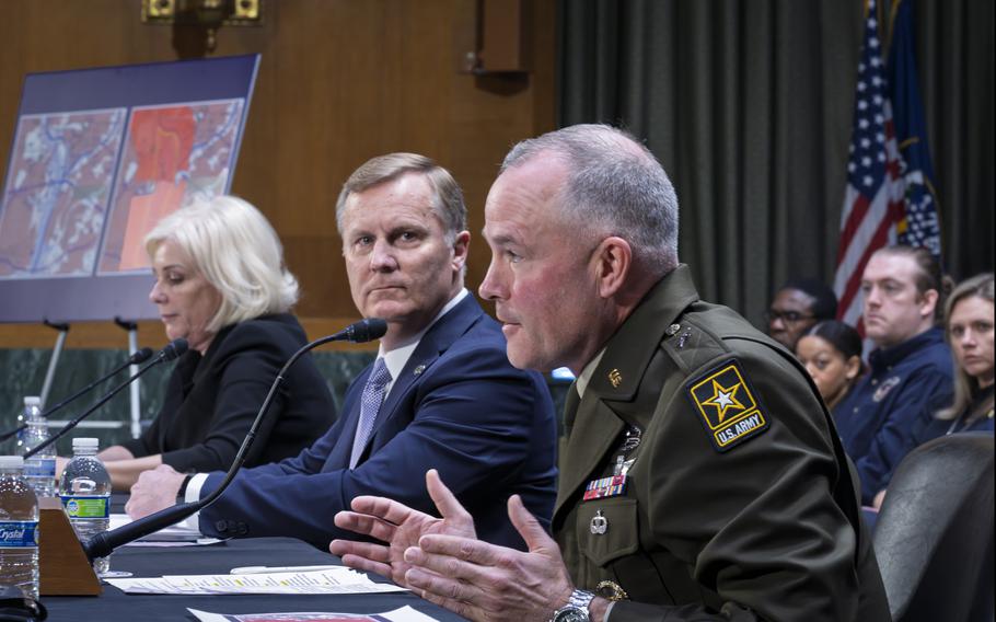 A man in an Army uniform gestures as he speaks into a microphone on a table.