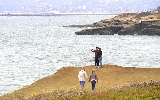 People walk along a cliff next to the ocean.