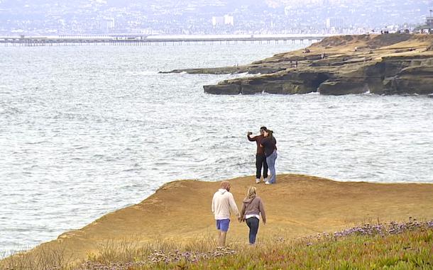 People walk along a cliff next to the ocean.