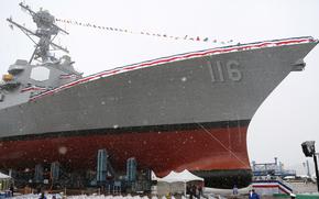 A naval destroyer with a red, white and blue ribbon along its rail sits next to a dock.