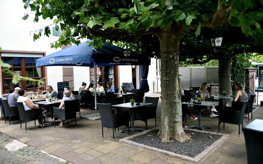 Diners sit on the patio, under trees at an Italian restaurant. 