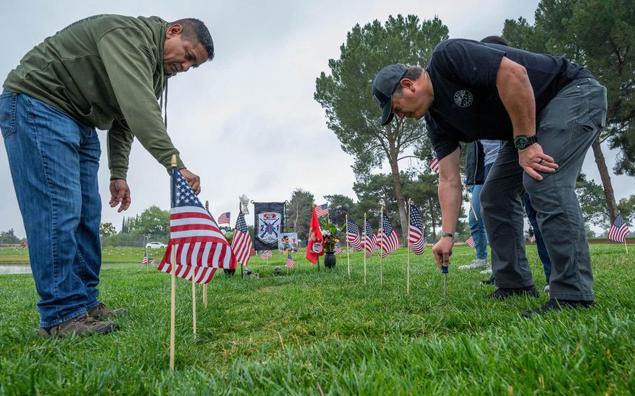 From left, Rene Santos helps Herman Lopez place flags around U.S. Marine Corps Cpl. Hunter Lopez’s grave as they volunteer with hundreds of others to place 250,000 flags at Riverside National Cemetery for Monday’s observance of Memorial Day in Riverside on Saturday, May 28, 2022.