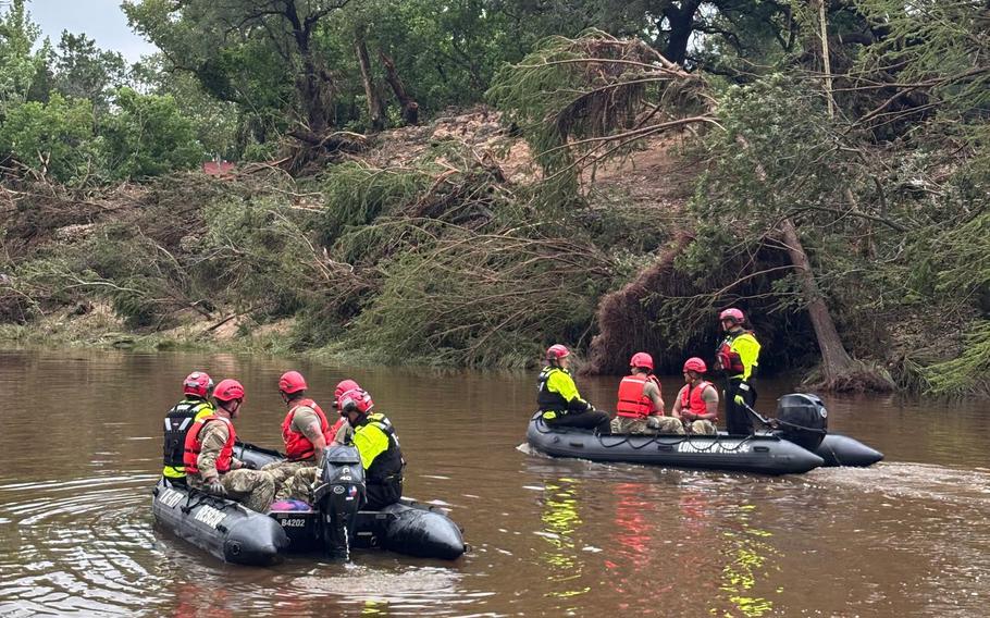 Troops on motorized rafts search a river.