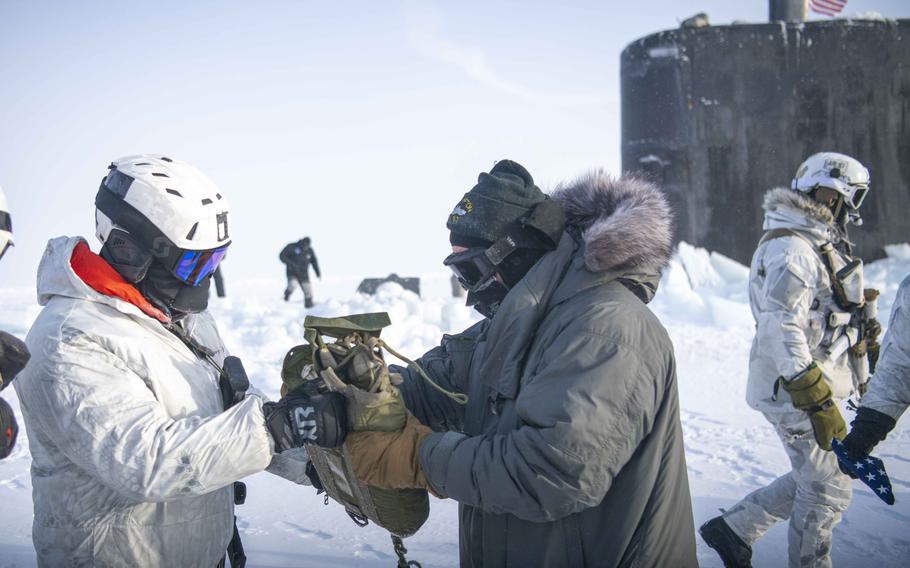 A Navy special warfare operator hands off a package from an airdrop to a sailor assigned to the attack submarine USS Hampton on Saturday, March 9, 2024, during an integration exercise that was part of Arctic Edge 24.