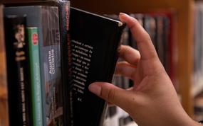 A close-up view of a hand taking a black-covered book from a library shelf.