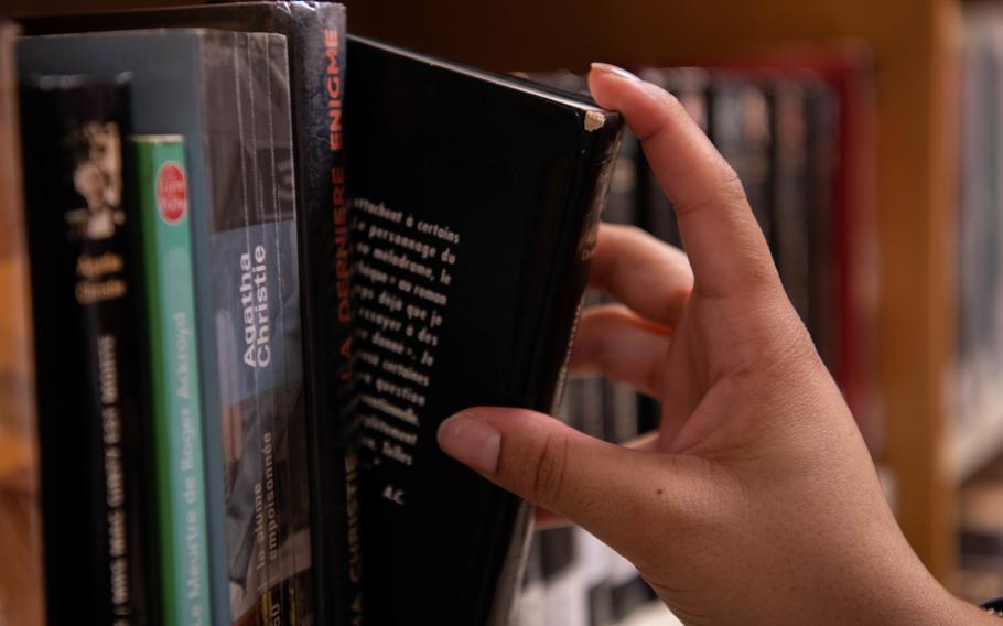 A close-up view of a hand taking a black-covered book from a library shelf.